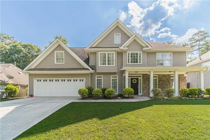 Two-story exterior with neutral siding, a covered front porch with stone accents, a two-car garage, and a concrete driveway