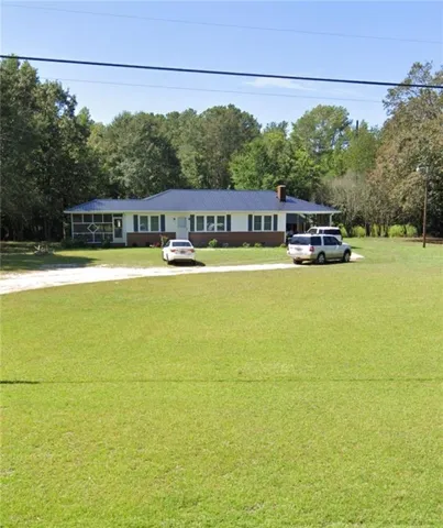 Ranch-style residence featuring a dark blue metal roof, white siding, and a brick foundation