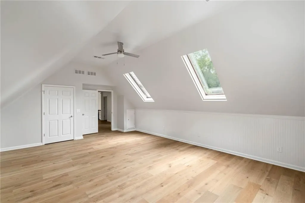 Additional living space featuring lofted ceiling with skylight, ceiling fan, and light hardwood / wood-style floors