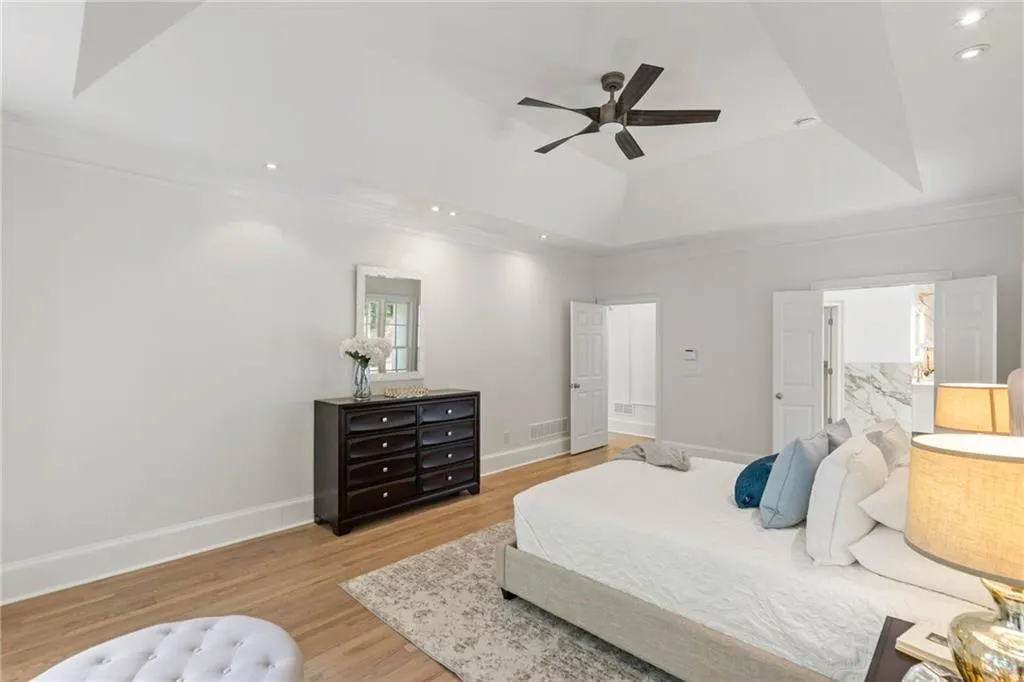 Bedroom with light wood-type flooring, crown molding, ceiling fan, and a raised ceiling