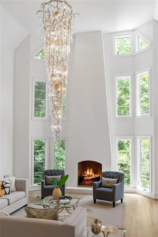 Living room with a towering ceiling, a notable chandelier, light wood-type flooring, and a healthy amount of sunlight