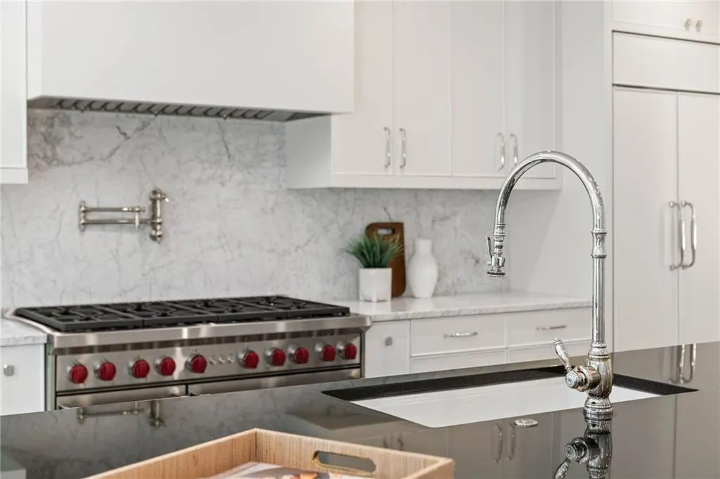 Kitchen with backsplash, stone countertops, double oven range, and white cabinetry