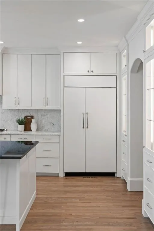 Kitchen with paneled fridge, white cabinets, light hardwood / wood-style floors, and backsplash