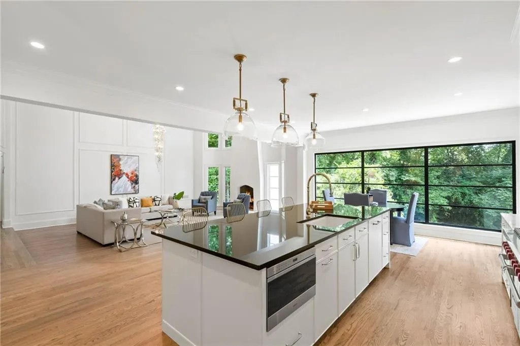 Kitchen with white cabinets, hanging light fixtures, a center island with sink, ornamental molding, and light wood-type flooring