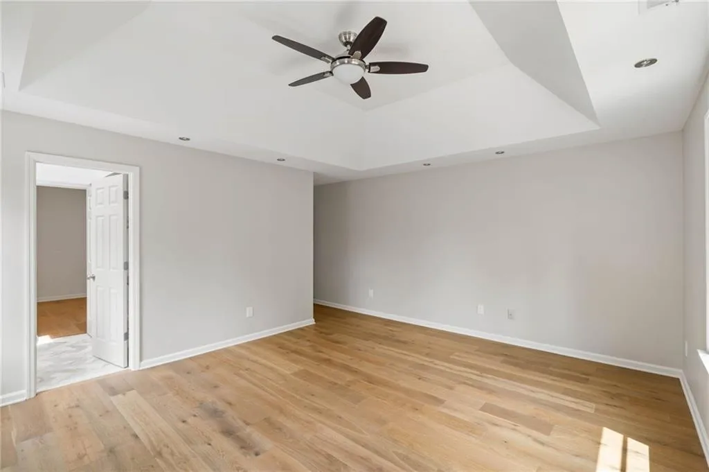 Empty room featuring light wood-type flooring, ceiling fan, and a raised ceiling