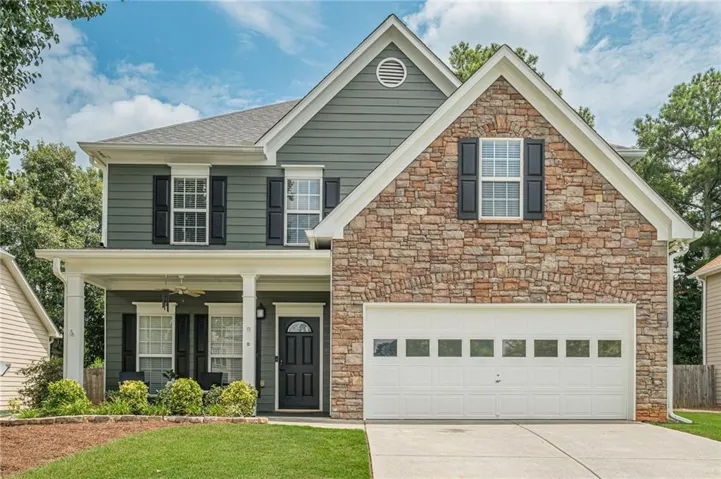 Two-story brick and siding home featuring a welcoming front facade with multiple windows, a two-car garage with paneled doors, and a manicured lawn with mature landscaping