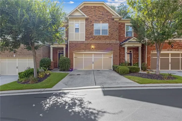 Brick and stone facade with a portico entry, concrete driveway, attached two-car garage, and established front landscaping