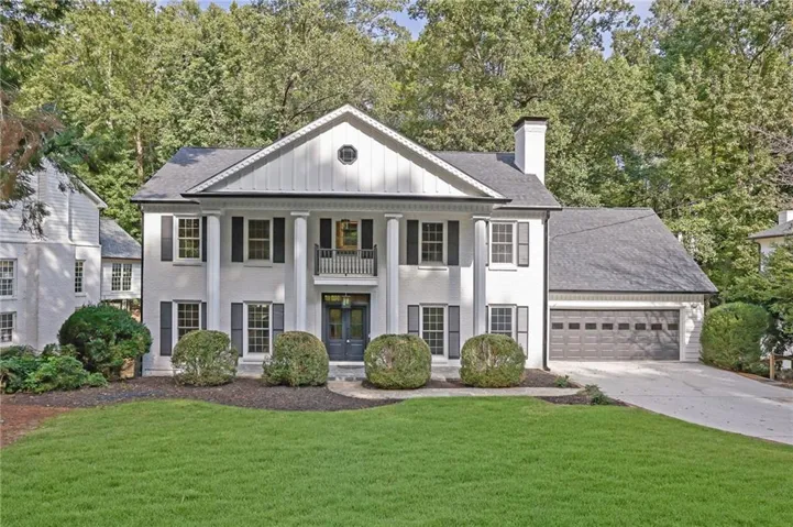 Colonial-style exterior featuring a portico with columns, an upper-level balcony, a two-car garage, and mature landscaping