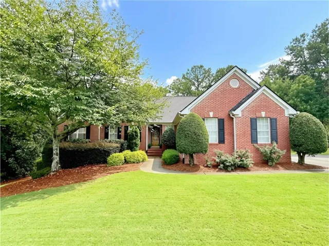 Charming brick residence showcasing a manicured front lawn, mature landscaping with professionally trimmed hedges, and a circular driveway