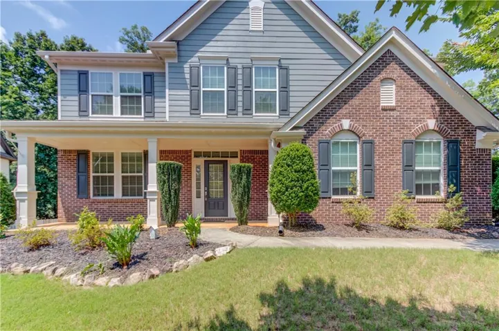 Two-story residential exterior featuring brick and horizontal siding, a covered porch with white columns, a dark panel front door with transom window, and a manicured lawn with landscaping