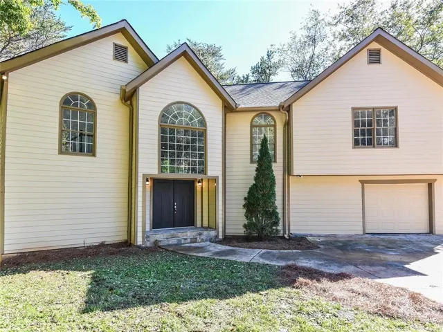 Exterior facade featuring a prominent arched window above double entry doors, horizontal siding, and a two-car garage