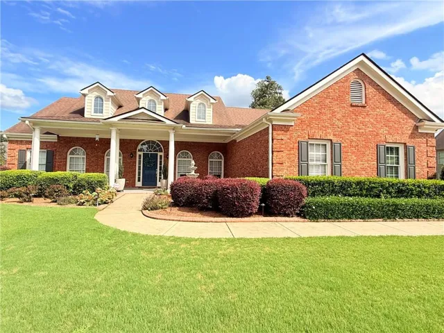 Red brick exterior with white columns, a blue front door, dormer windows, and a manicured lawn