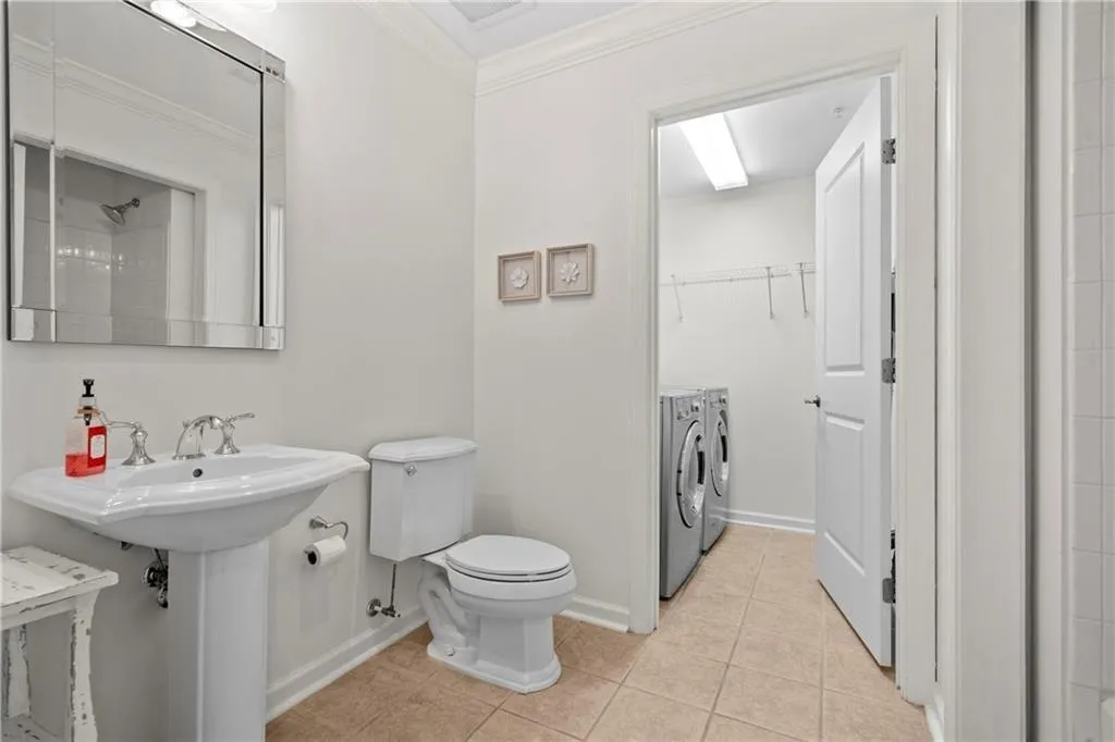 Bathroom featuring tile patterned flooring, washer and dryer, toilet, walk in shower, and crown molding