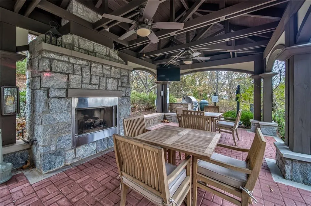 View of patio / terrace featuring ceiling fan, area for grilling, a grill, and an outdoor stone fireplace and grilling area.
