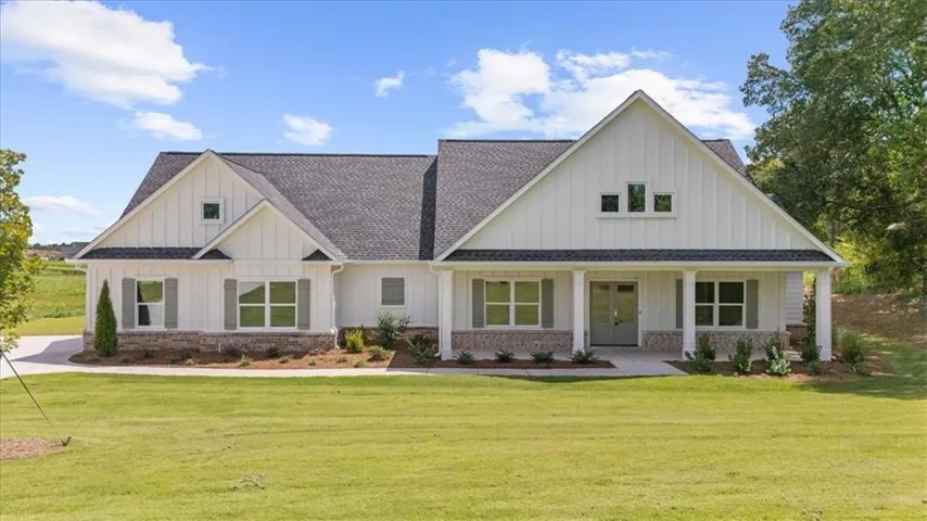 Board and batten siding, brick skirting, covered front porch, gabled rooflines, and a paved driveway