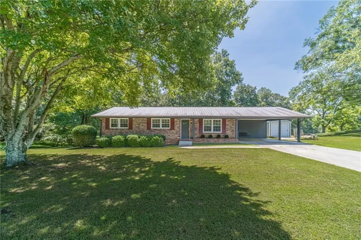Brick ranch home set on expansive manicured grounds beneath mature shade trees, featuring a modern addition with extended roofline, multiple windows for natural light, and a concrete driveway approach