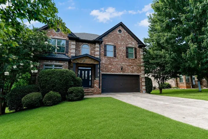Brick facade residence featuring a covered entry, dark garage door, and mature landscaping