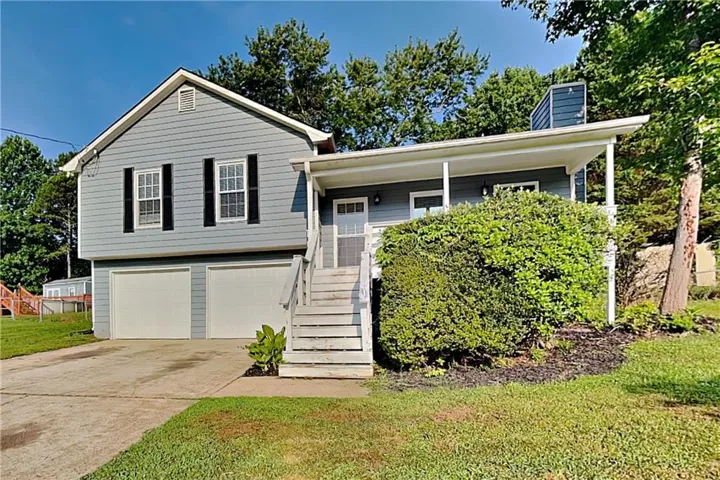 Split-level home featuring light blue siding with white trim, a covered porch entry, and an attached two-car garage