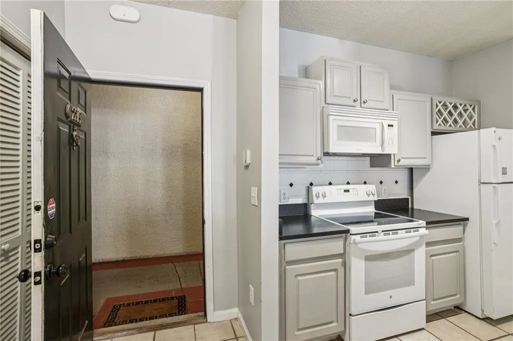 Kitchen with white appliances, dark countertops, light tile patterned floors, backsplash, and a textured ceiling