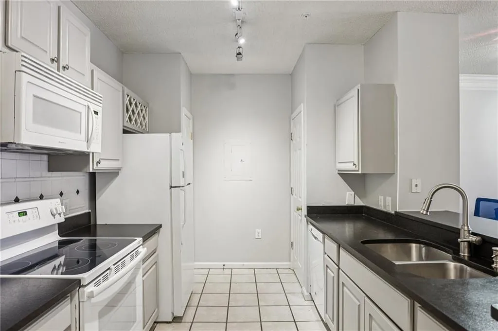 Kitchen featuring white appliances, light tile patterned floors, a textured ceiling, white cabinets, and decorative backsplash