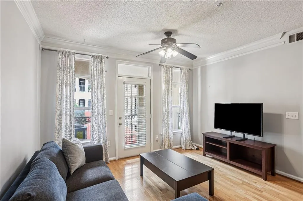 Living area with a textured ceiling, crown molding, light wood finished floors, and a ceiling fan