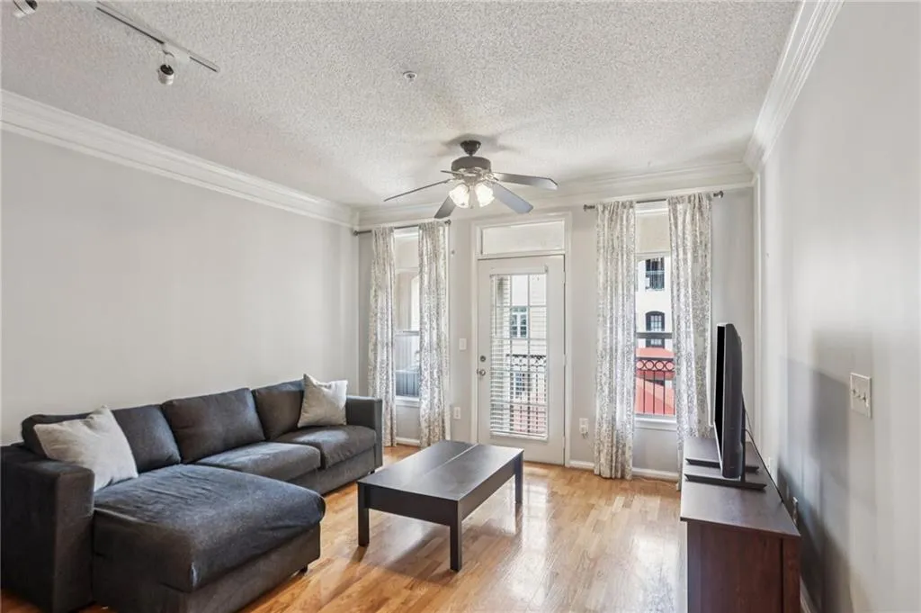 Living area with a textured ceiling, light wood-type flooring, ornamental molding, a ceiling fan, and track lighting