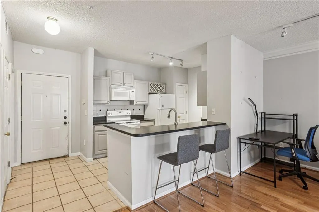 Kitchen with track lighting, a kitchen bar, backsplash, white appliances, and a textured ceiling