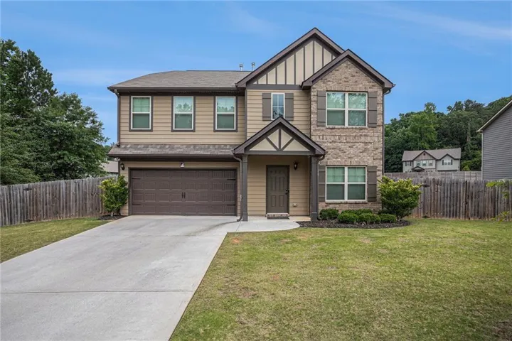 Two-story residence featuring a brick and siding exterior, an attached garage, a paved driveway, a manicured lawn, and mature perimeter fencing