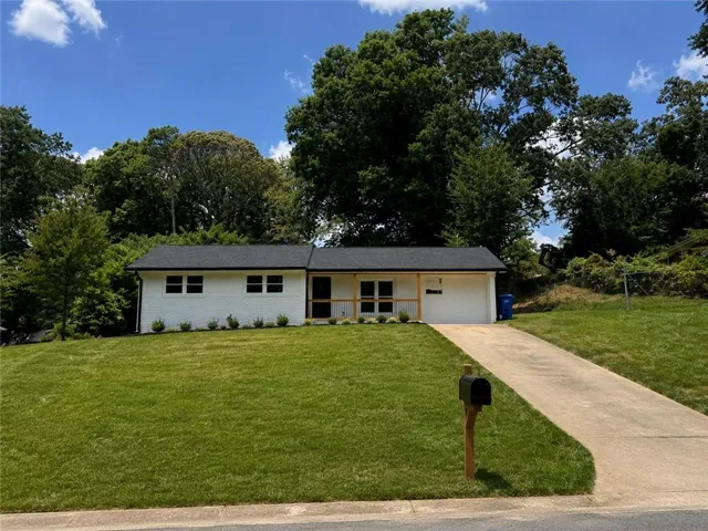 White single-story exterior with a dark shingle roof, attached single-car garage, concrete driveway, and a front lawn with foundational plantings