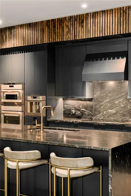 Kitchen featuring sink, backsplash, dark stone counters, stainless steel double oven, and a kitchen breakfast bar