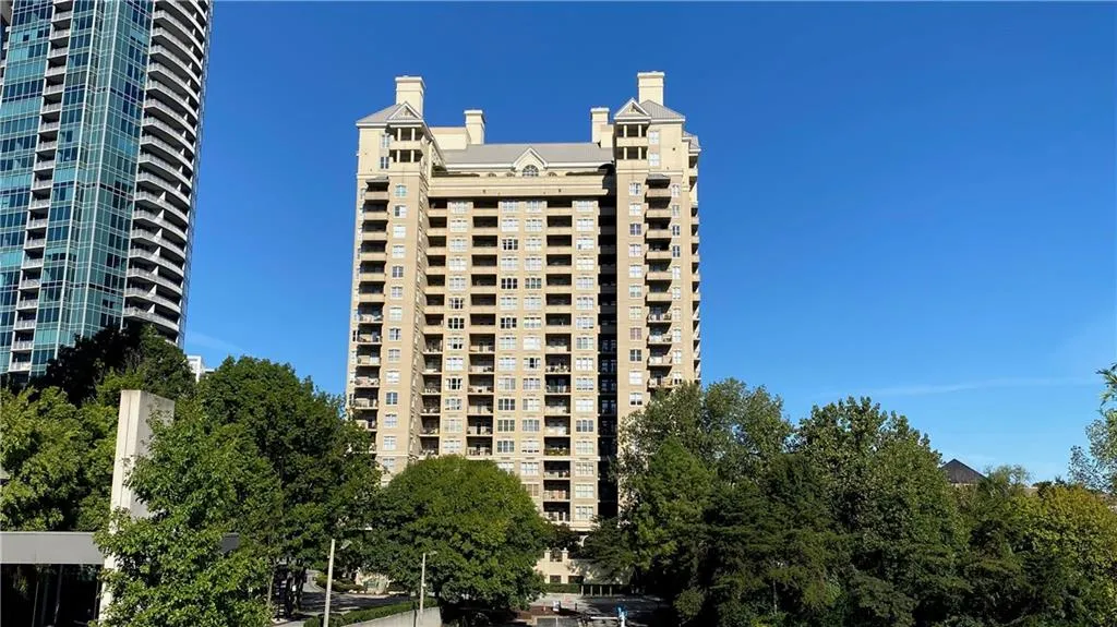 High-rise building with multiple balconies, a light-toned facade, and architectural roof detailing