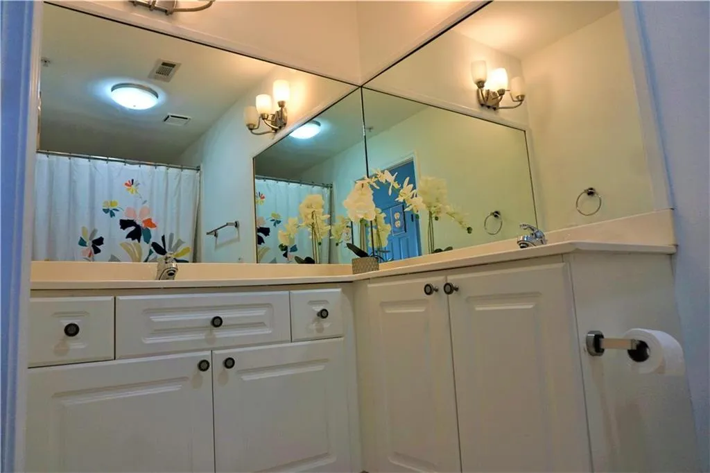 Dual vanity with white cabinetry and integrated sinks, wall-mounted mirrors, and sconce lighting