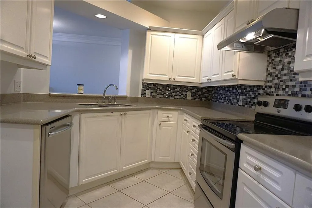 White shaker cabinetry, mosaic tile backsplash, stainless steel appliances, dual basin sink, and tile flooring