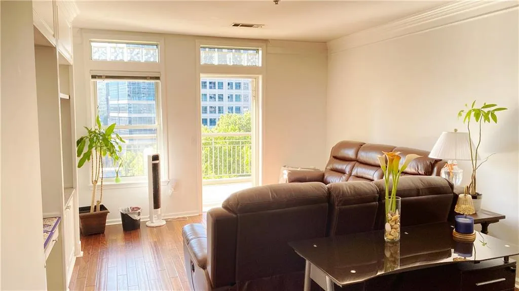 Crown molding enhancing ceiling lines, built-in shelving, wood-finish flooring, balcony access, and large windows providing abundant natural light
