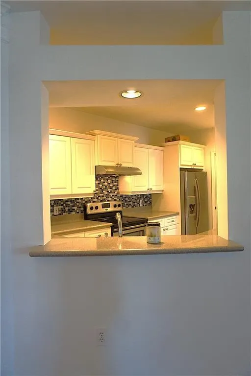 Kitchen pass-through with a stone countertop, white cabinetry, mosaic tile backsplash, and stainless steel appliances