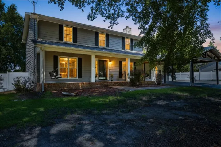 Modern farmhouse exterior with a two-story design featuring board-and-batten siding, a covered front porch with substantial columns, and dormer windows with black shutters
