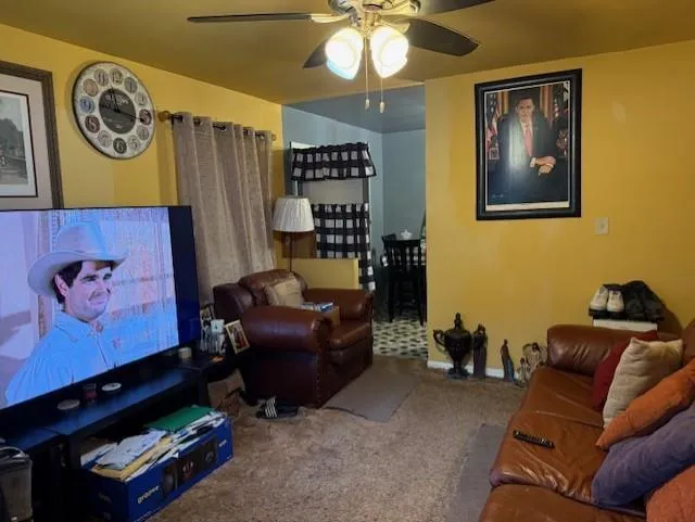 Carpeted living area featuring ceiling fan and baseboards