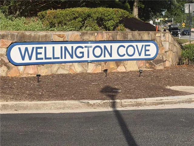 Community entrance sign for Wellington Cove featuring a stone base and lush landscaping