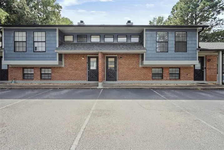 Two-story building exterior featuring brick and blue siding, multiple windows, and a paved parking area