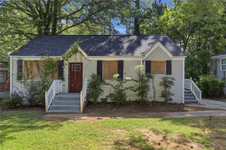 White brick exterior, black shingle roof, red entry door with window pane, white porch railings, and a concrete front porch