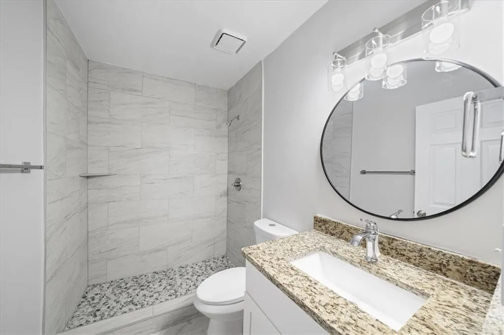 Full bathroom featuring toilet, tiled shower, and vanity