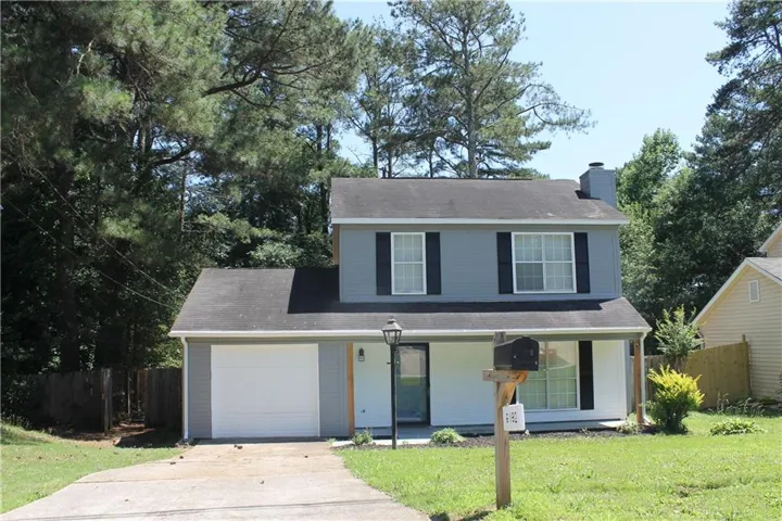Two-story home featuring a light gray and white exterior with dark shutters, a front-facing garage, and a concrete driveway