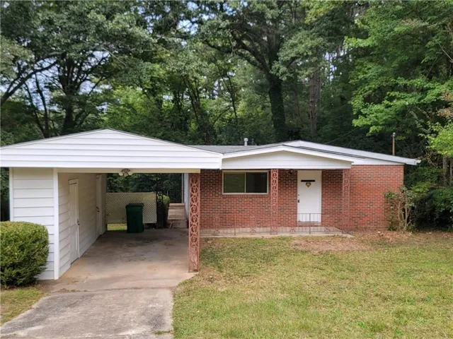 Brick exterior with a white entry door, carport, and a concrete driveway