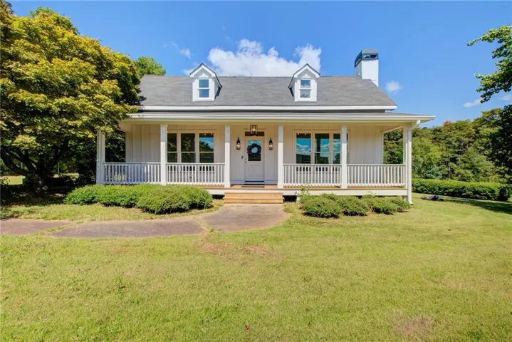White farmhouse-style residence featuring a broad front porch with white railings, a dark shingle roof, and twin dormer windows