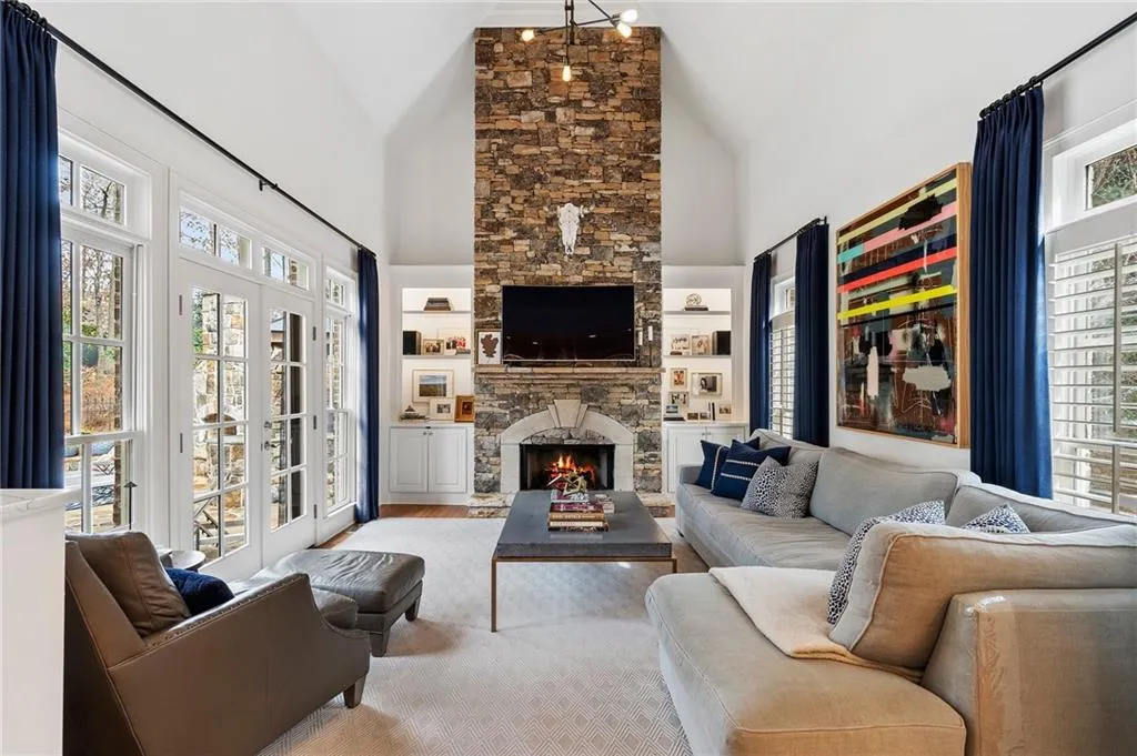 Living room with a stone fireplace, a healthy amount of sunlight, and high vaulted ceiling