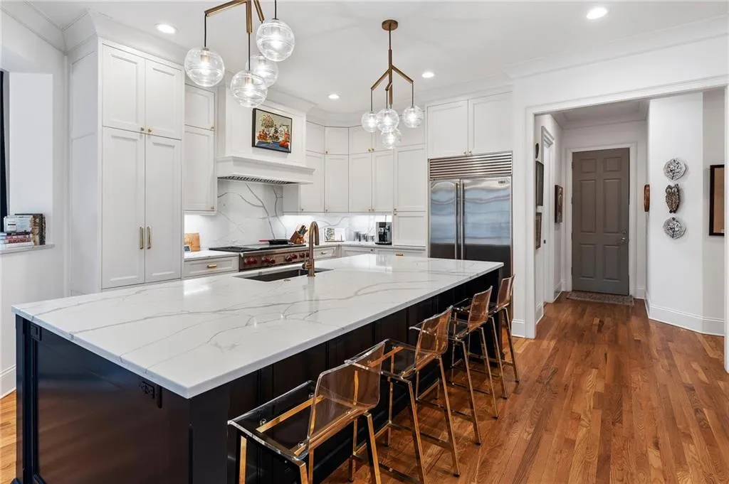 Kitchen with white cabinets, decorative backsplash, hanging light fixtures, a large island, and light stone counters