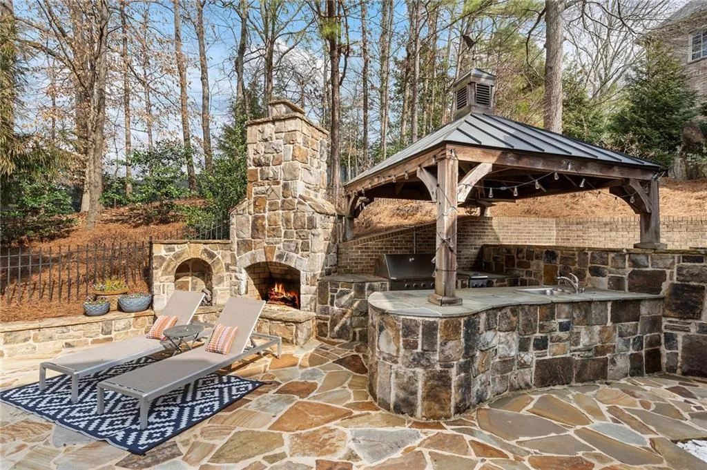 View of patio with an outdoor kitchen, a grill, sink, an outdoor stone fireplace, and a gazebo