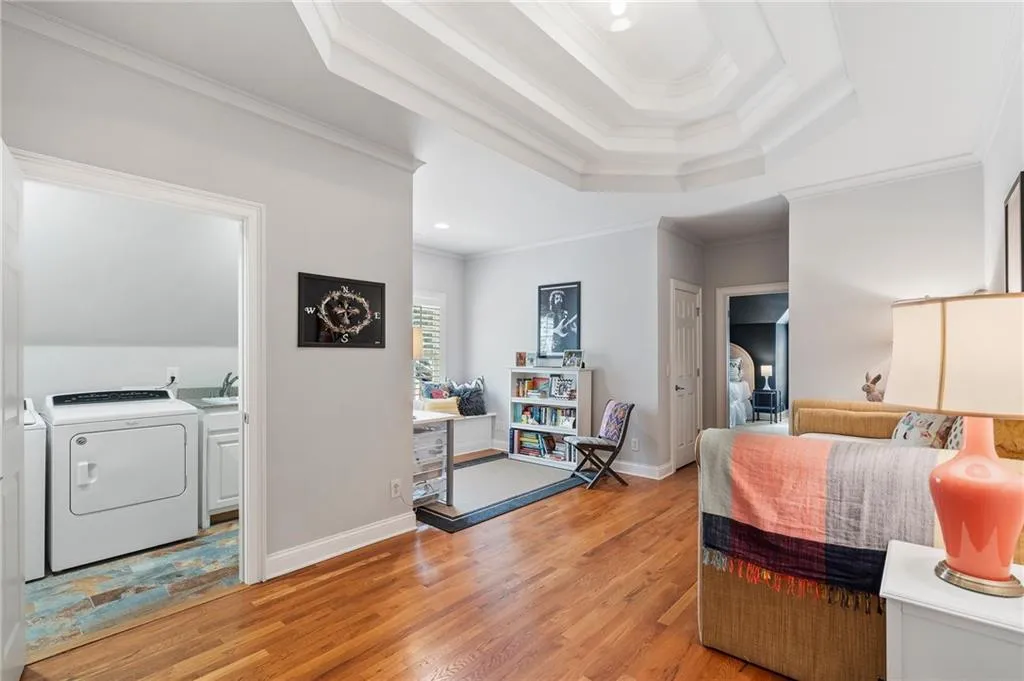 Bedroom with crown molding, a tray ceiling, washer and clothes dryer, and light wood-type flooring