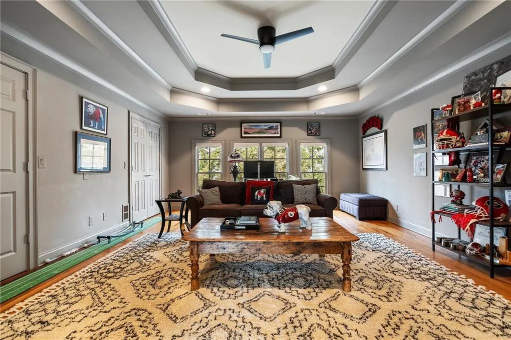 Living room featuring a raised ceiling, crown molding, ceiling fan, and light hardwood / wood-style flooring