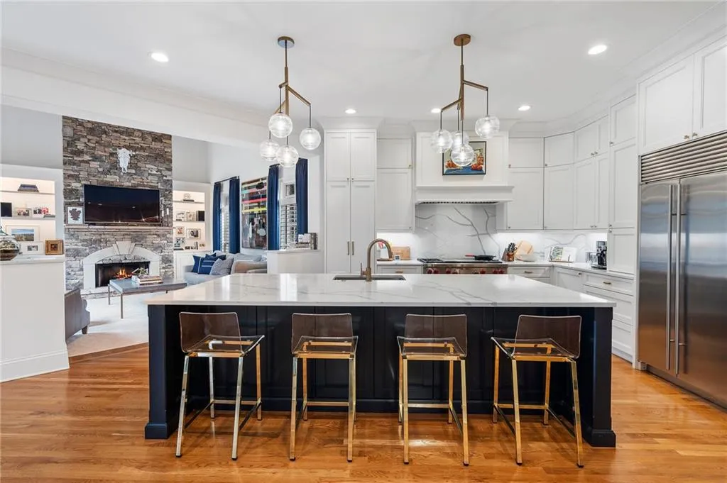 Kitchen with white cabinetry, hanging light fixtures, a center island with sink, and stainless steel built in refrigerator